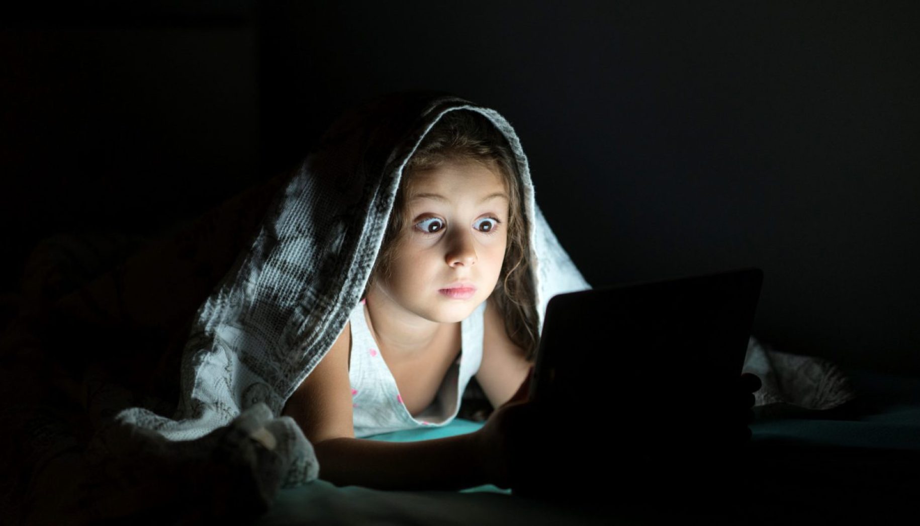 Little girl using digital tablet in her bed at night